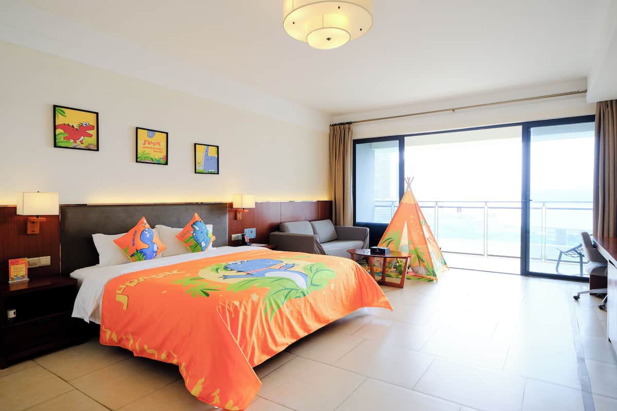 Habitación de hotel con una cama grande, un escritorio, una silla, un ventanal con vistas y un balcón.