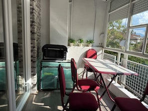 Un balcon avec un four à micro-ondes VIMAX noir, des chaises rouges, une table blanche et des plantes en pot.