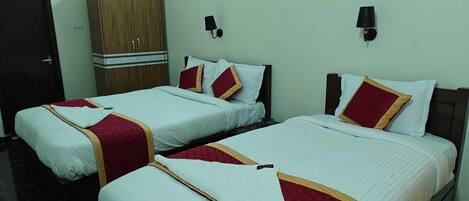 A hotel room with two beds, each with white bedding and red accents, a wooden wardrobe, and wall-mounted lamps.