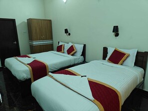 A hotel room with two beds, each with white bedding and red accents, a wooden wardrobe, and wall-mounted lamps. - Royal Parisian Residency (Pattukkottai)