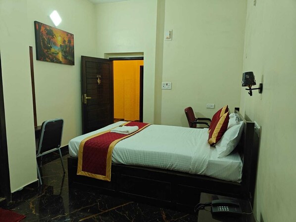 Un dormitorio con cama, escritorio, silla, un cuadro y una puerta.