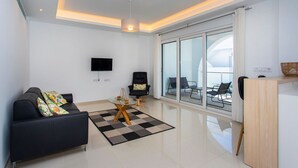 A modern living room with a black sofa, a glass coffee table, and a black and white rug. There is a TV mounted on the wall, a chair, and a balcony with chairs. - CH Enora Garden Doña Pepa (Ciudad Quesada) (Ciudad Quesada)