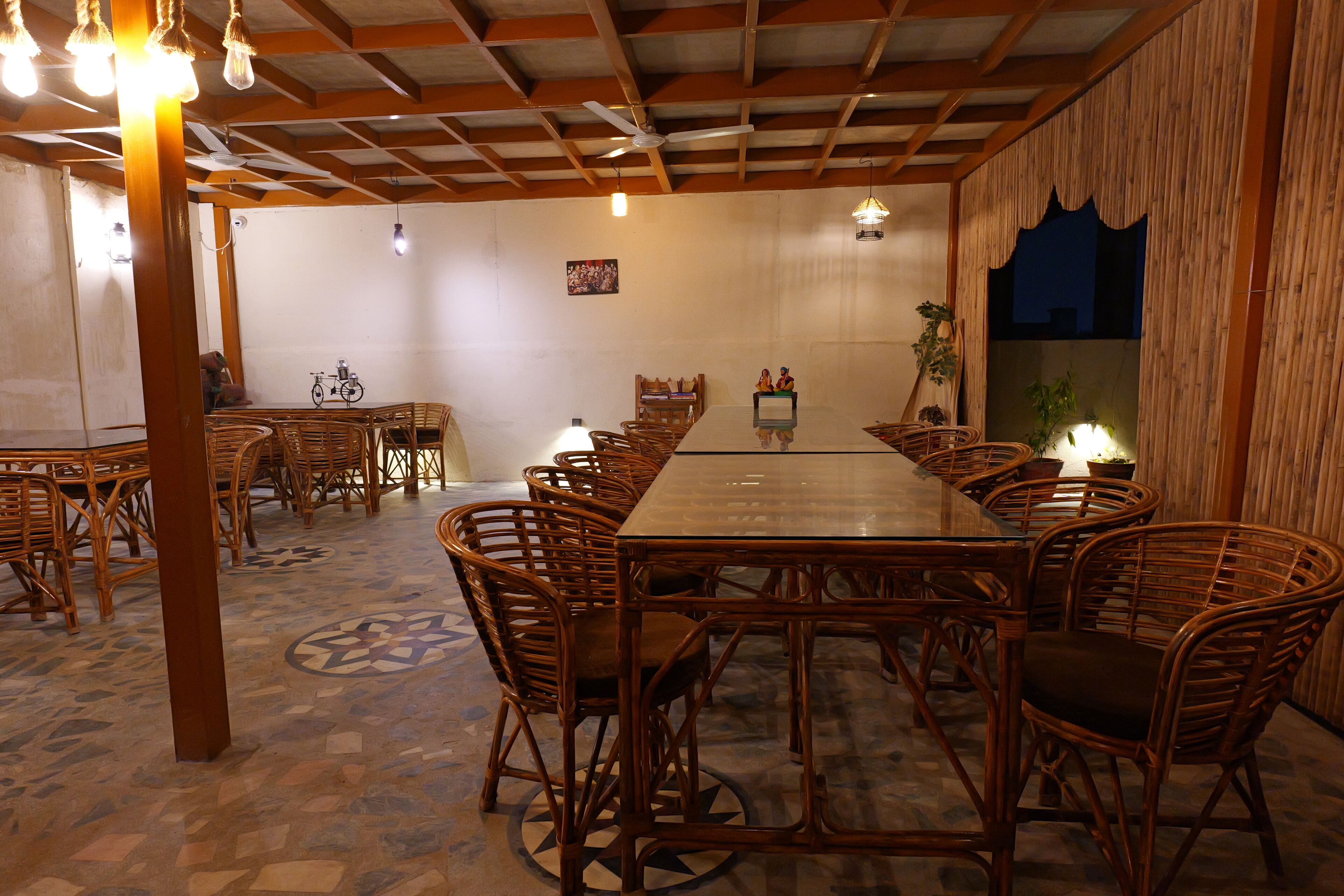 A dining area with a long wooden table surrounded by wicker chairs, a ceiling fan, and hanging light fixtures.