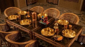 Een klassieke eettafel gedekt voor meerdere personen, met gouden borden, bekers en een messing karaf.