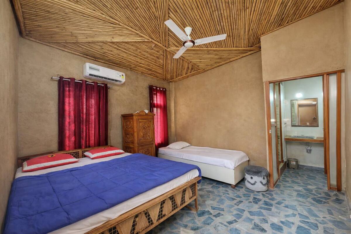 Quarto com duas camas, ventoinha no teto, ar condicionado e um banheiro pequeno.