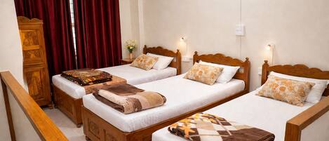 A hotel room with three wooden beds, a wooden wardrobe, and a red curtain.