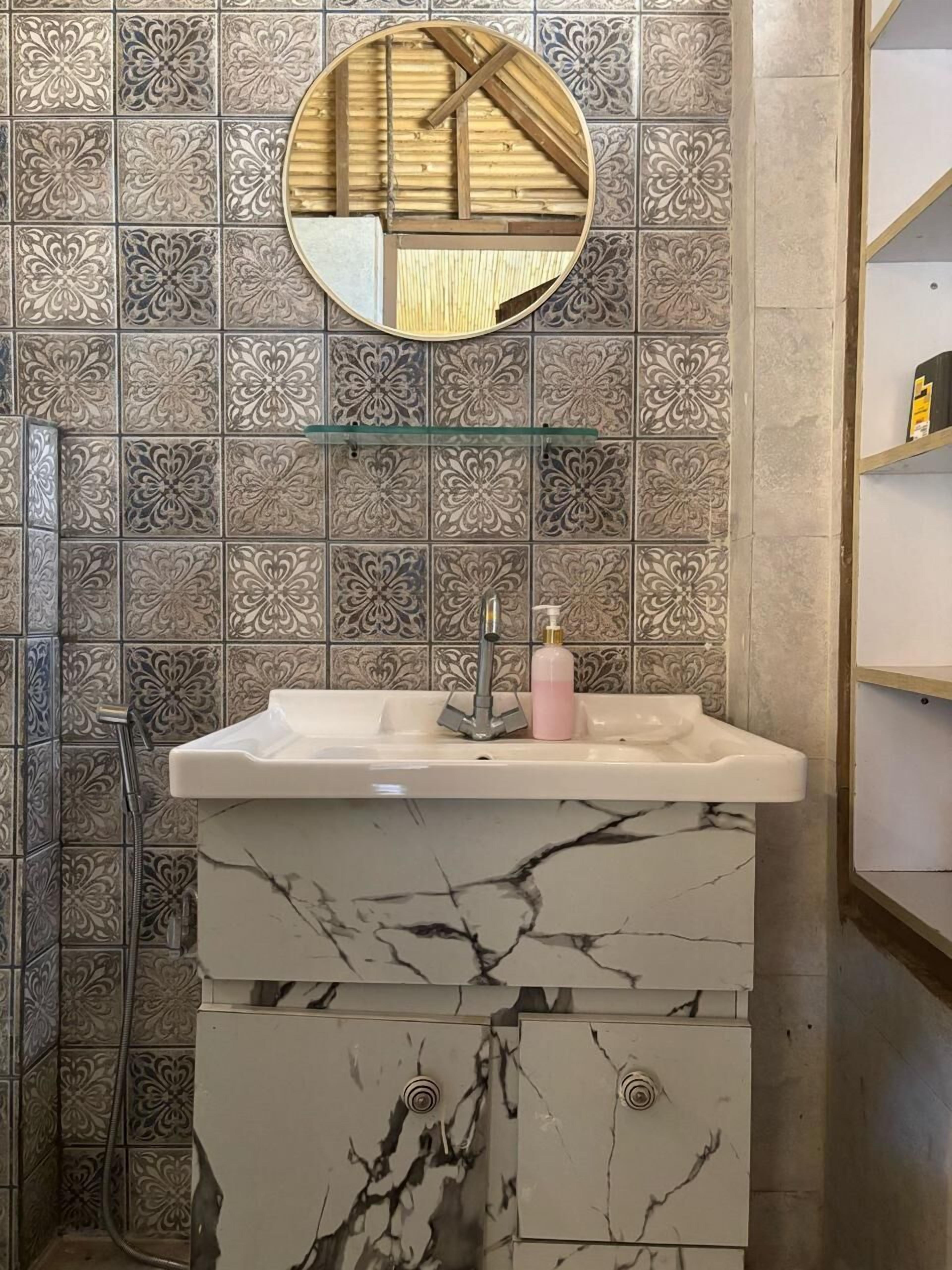 A bathroom with a marble sink, a glass shelf, a mirror, and patterned tiles.