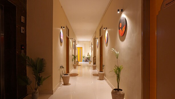 Een hotelgang met een gepoetste vloer, potplanten en kunstwerken in lijsten aan de wanden.