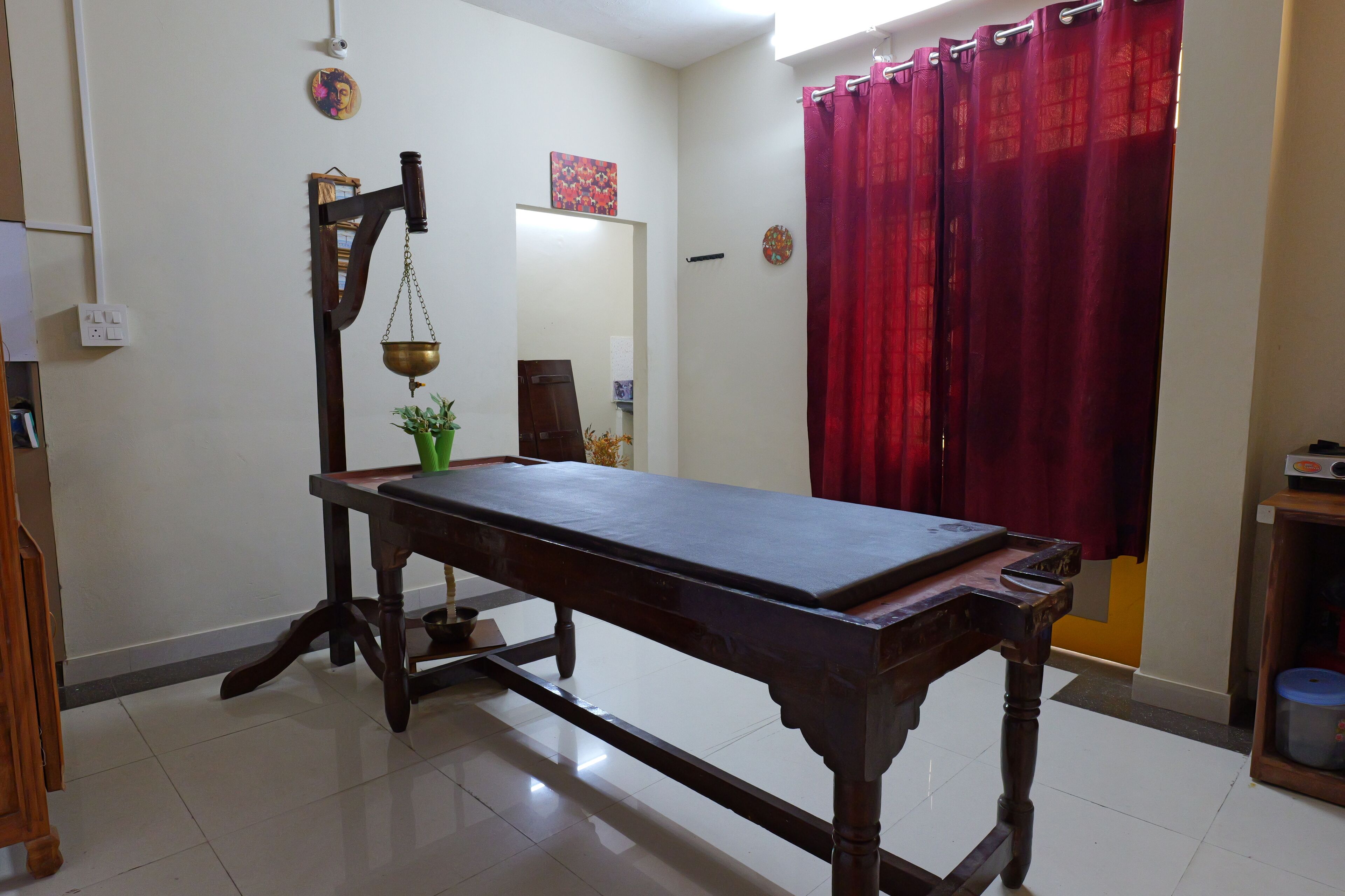 A room with a wooden table, a hanging scale, and a red curtain.