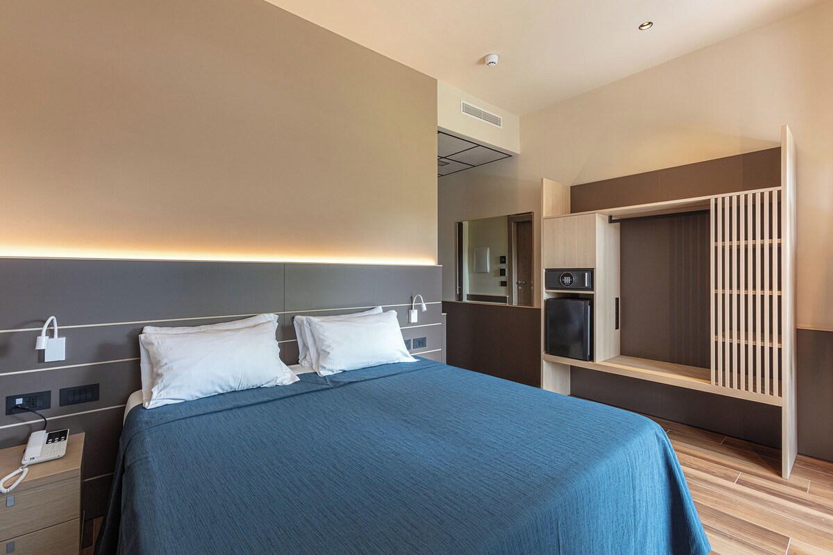 A hotel room with a bed, bedside controls, a telephone, a wardrobe, and a mirror.