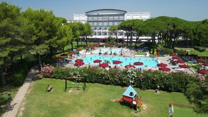 Una gran piscina al aire libre rodeada de sombrillas rojas, una zona de juegos infantiles y un edificio al fondo.