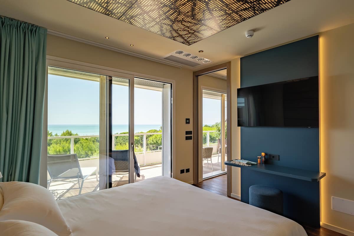Un dormitorio con una cama grande, un televisor montado en la pared y un balcón con vista al mar.