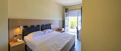 Ein Hotelzimmer mit einem großen Bett, Nachttischen, einem Schreibtisch und einer Glastür zum Außenbereich.