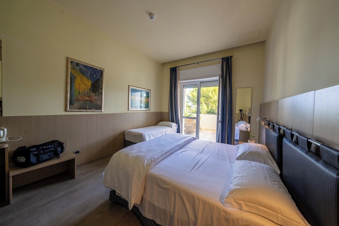 A hotel room with two beds, a desk with a chair, a window, and a painting on the wall.