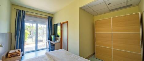Een hotelkamer met een bed, een bureau met een computer, een kledingkast en een schuifdeur naar buiten.