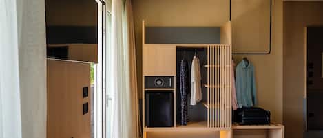 A modern hotel room with a bed, a small desk, a wardrobe, and a mini-fridge.