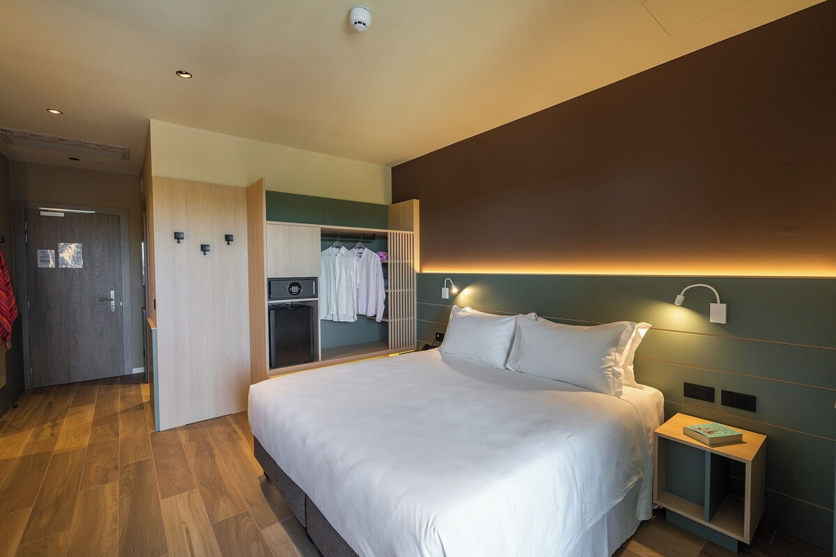 Een moderne hotelkamer met een groot bed, een kledingkast en een nachtkastje met een boek.