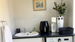 A compact kitchen with a sink, a coffee machine, a washing machine, and a framed picture on the wall.