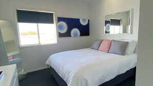 A modern bedroom with a bed, a large window, a wall-mounted mirror, and a ceiling vent.