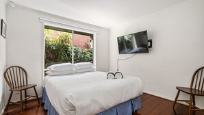 Une chambre à coucher comprenant un lit, deux chaises, un téléviseur et une fenêtre donnant sur un paysage verdoyant.