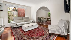 Un salon avec un canapé blanc, un fauteuil à rayures et une table basse. Un tapis rouge à motifs est posé sur le sol.