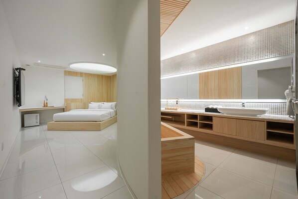 A modern hotel room with a large bed, a wooden platform, a large mirror, and a modern bathroom with a large sink and wooden vanity. - Guwol Hotel Rondo (Incheon)