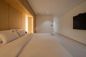 A modern hotel room with a large bed, a wooden panel wall, and a mounted TV.