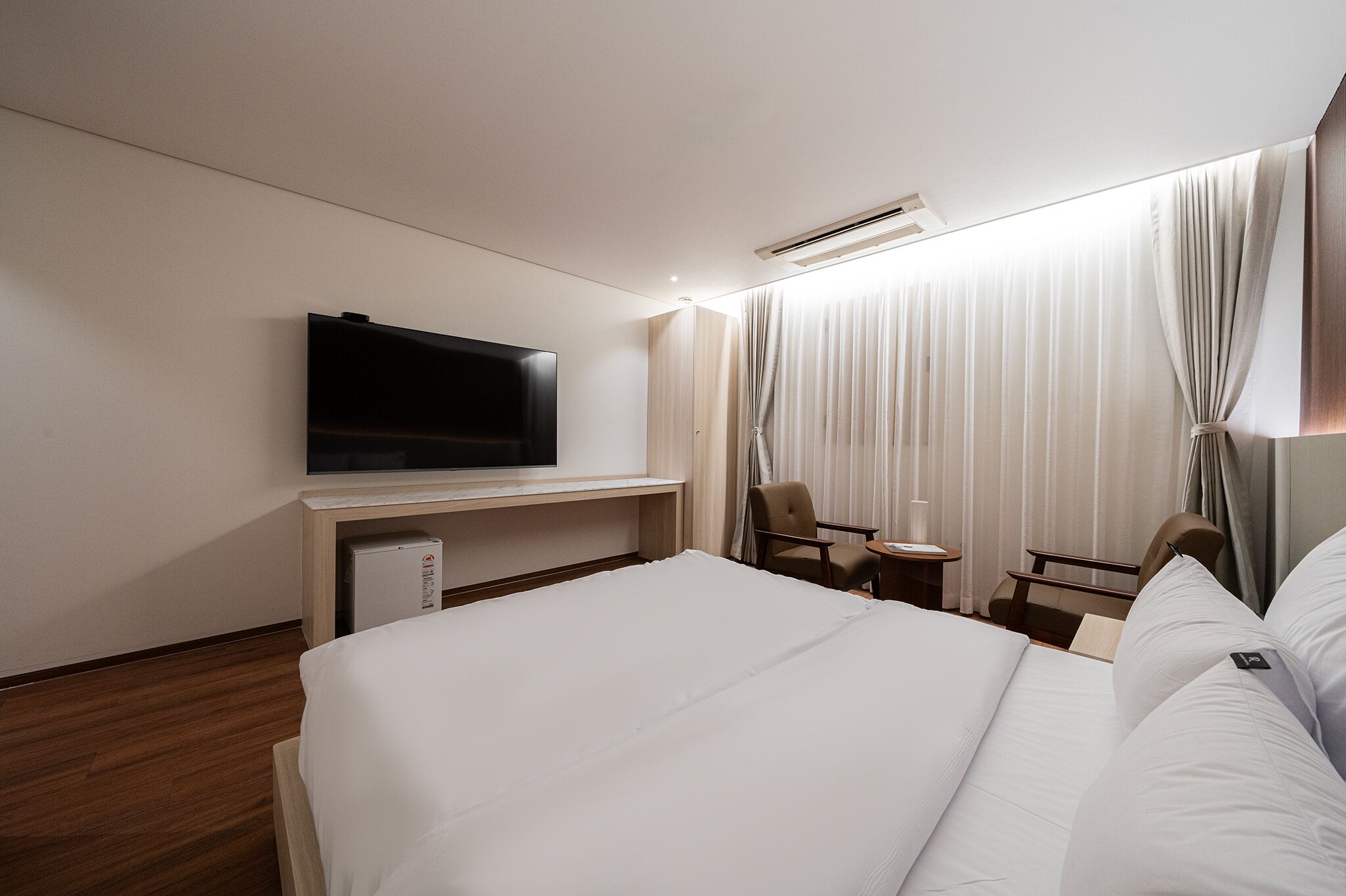 Habitación de hotel con una cama grande, un televisor de pantalla plana en la pared, una mesita con una silla y un escritorio con otra silla.