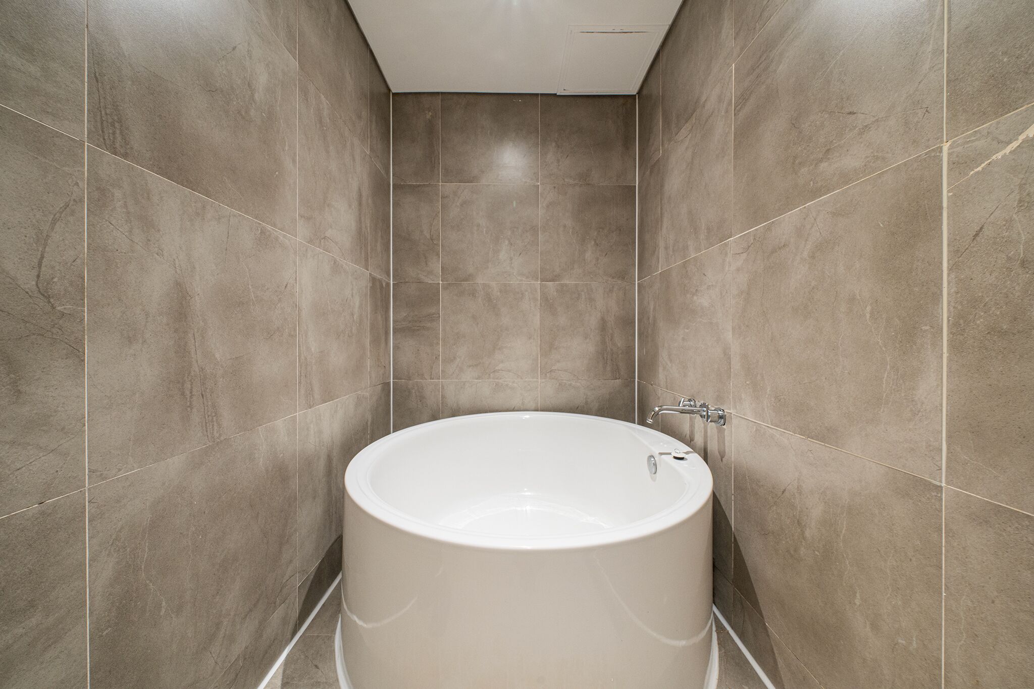 A modern bathroom with a freestanding bathtub, tiled walls, and a ceiling vent.