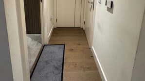 A hallway with wooden flooring, a black doormat, and white walls. - Cosy Riverview apartment. 10mins to the o2 Arena. (Woolwich)
