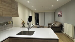 A modern kitchen with a central island, built-in wooden cabinets, and a large window. - Cosy Riverview apartment. 10mins to the o2 Arena. (Woolwich)