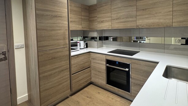 A modern kitchen with wooden cabinets, a white countertop, and built-in appliances. - Cosy Riverview apartment. 10mins to the o2 Arena. (Woolwich)