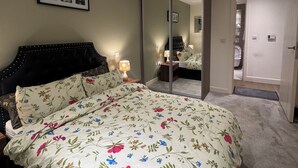 A bedroom with a bed, a bedside table, a mirror, and a door leading to a bathroom. - Cosy Riverview apartment. 10mins to the o2 Arena. (Woolwich)
