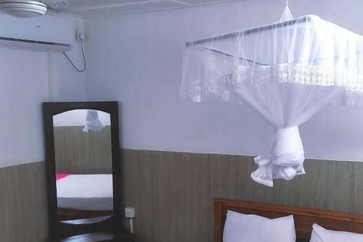 Un lit bien fait, avec une literie blanche et rose, une tête de lit en bois et un miroir au mur.