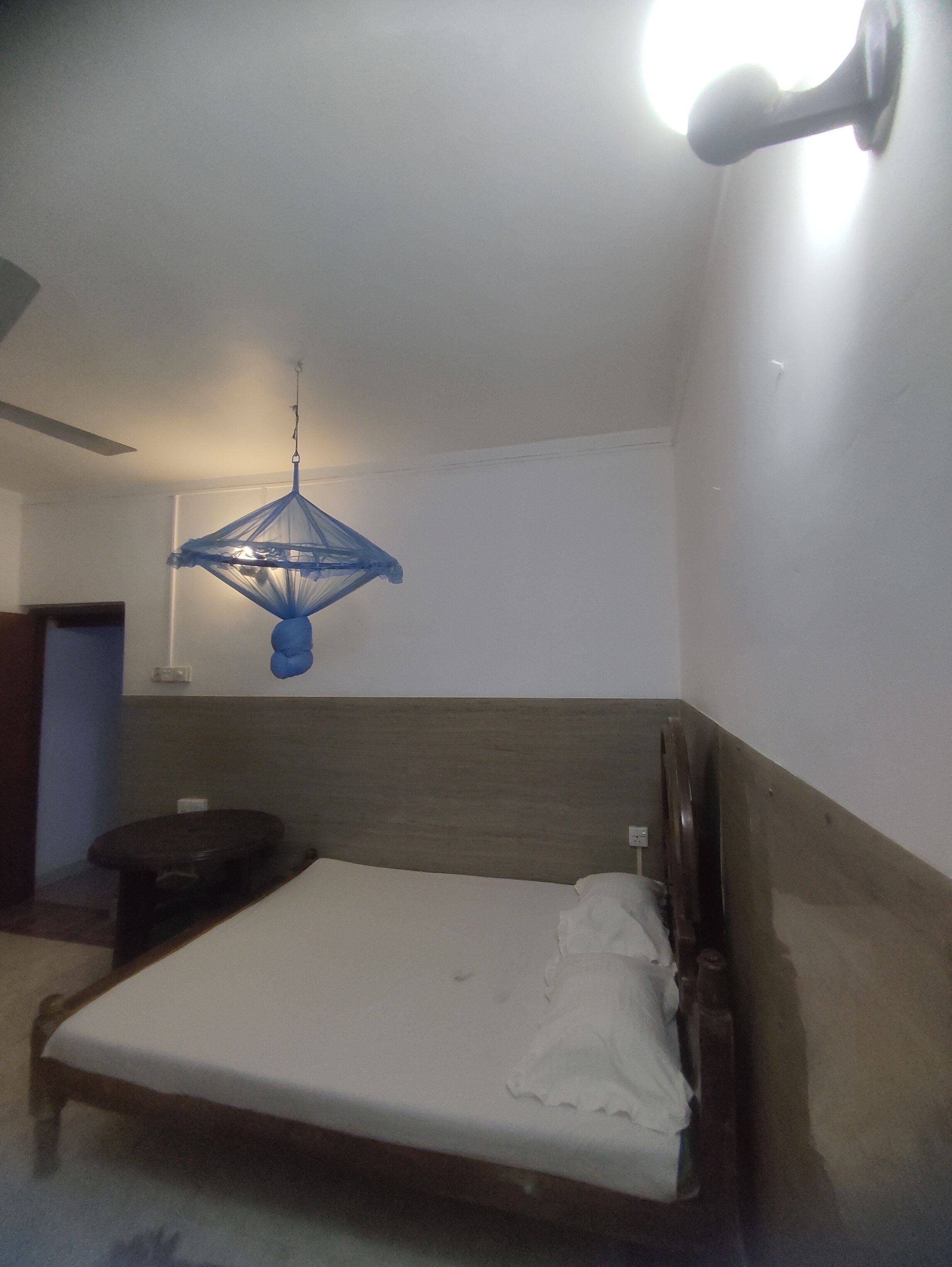 A bedroom with a single bed, a bedside table, a hanging blue light fixture, and a ceiling fan.