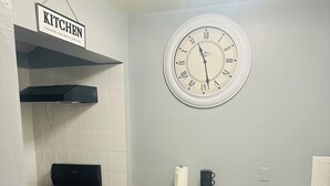 A compact kitchen with a gas stove, a clock, and a small dining table with two stools. - Odriozola’s Vrbo Studio (El Paso)