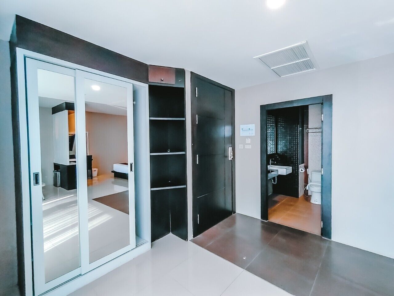 A modern hotel room with a sliding glass door leading to a bathroom, a built-in closet, and a separate bedroom area.