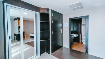 Habitación de hotel moderna con puerta corredera de vidrio que da al baño, armario empotrado y zona de dormitorio separada.