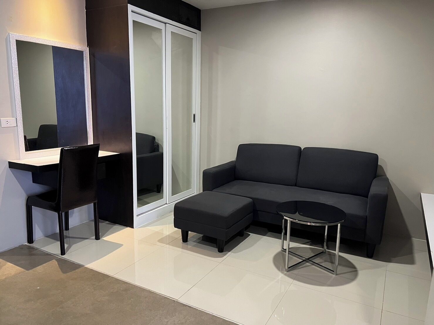 Een moderne woonkamer met een zwarte bank, een klein rond tafeltje en een zwarte stoel.