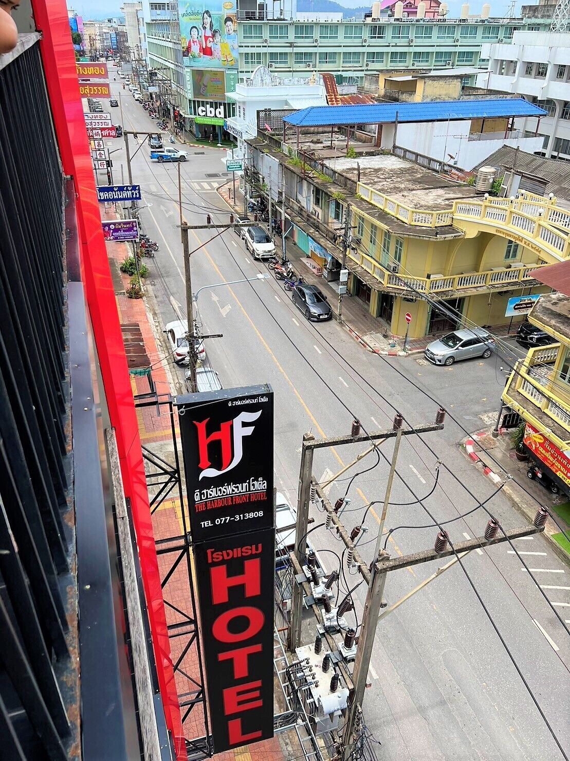 Une enseigne d’hôtel avec un logo rouge et noir, une vue de la rue avec des bâtiments, et un ciel dégagé.