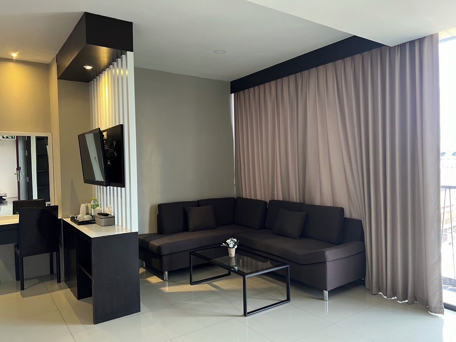 Un salon moderne avec un canapé foncé, une table basse en verre et un téléviseur à écran plat fixé au mur.
