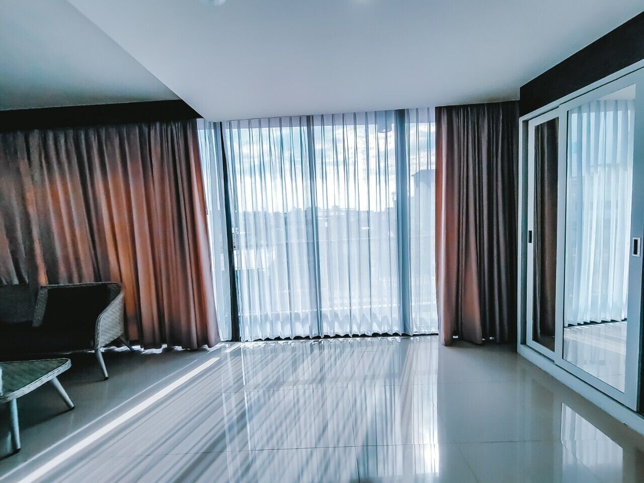 A modern hotel room with large sliding glass doors, a flat floor, and a seating area with a chair and a small table.