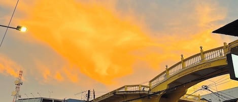 Un edificio amarillo con un puente peatonal, coches aparcados y una señal de tráfico.