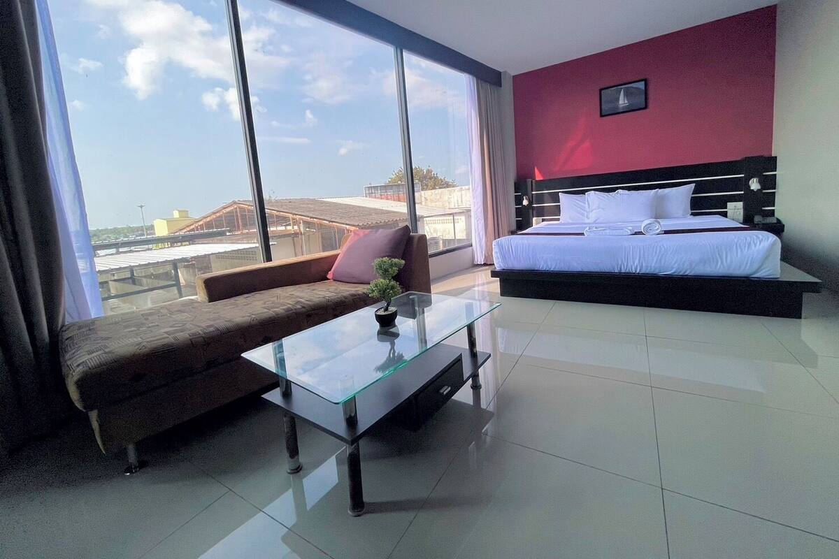 Una habitación de hotel moderna con una cama grande, una mesa de centro de vidrio, un sofá y vistas a la ciudad.