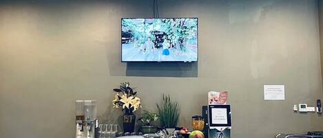 A conference room with a long table set for a meeting, a television screen, and a coffee station.