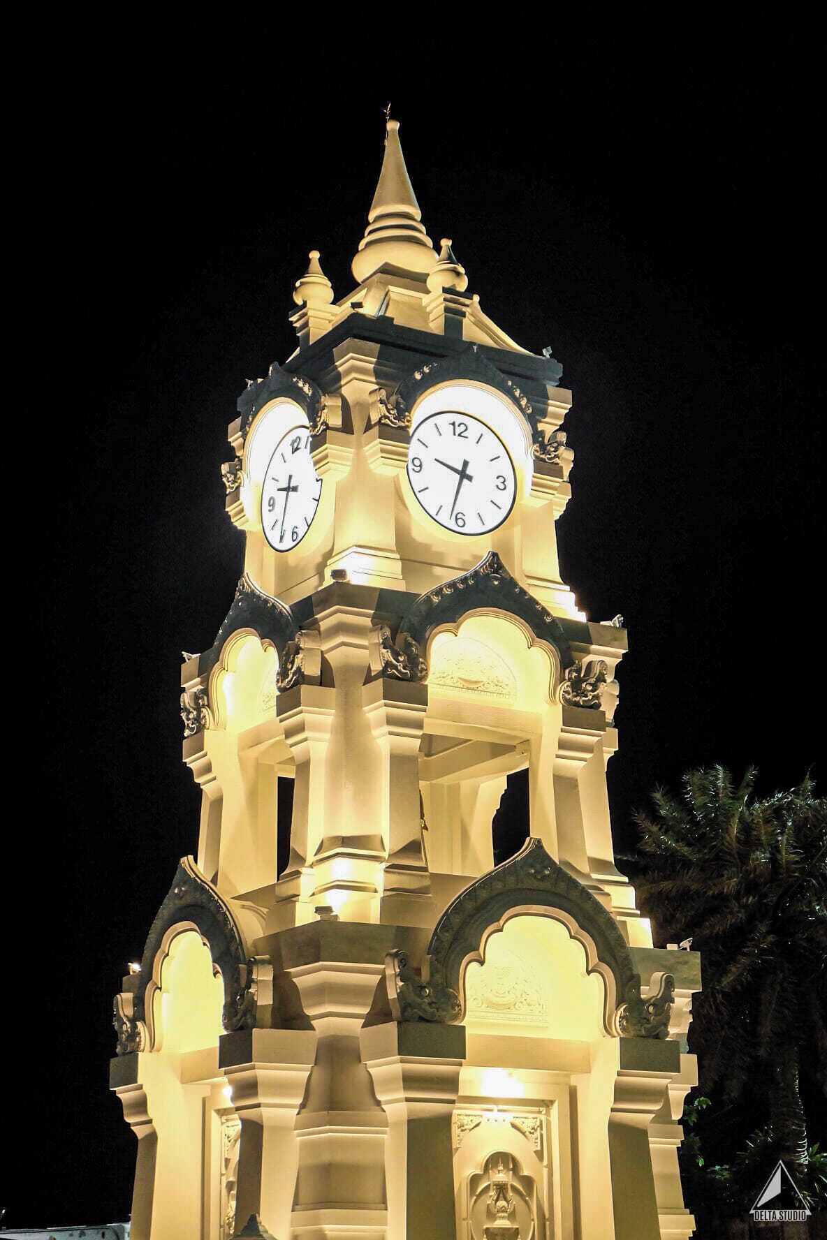 Uma torre do relógio com duas horas visíveis, detalhes arquitetônicos ornamentados e uma estátua na base.