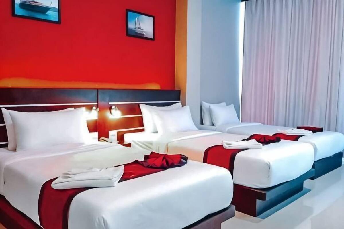 Habitación de hotel con dos camas, una pared de acento roja y un ventanal con cortinas.