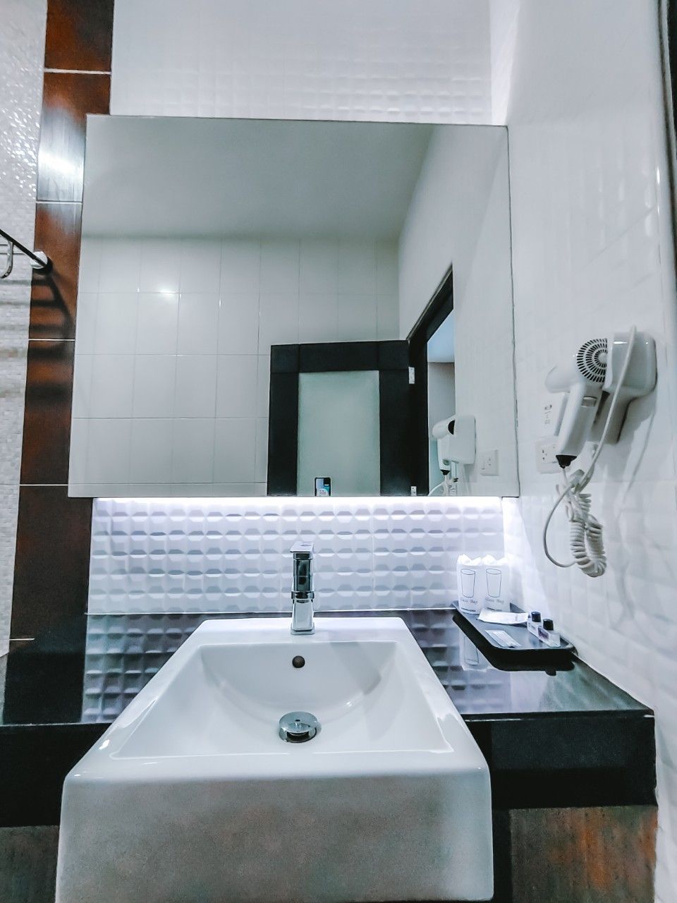 A modern bathroom with a large mirror, a white sink, and a hairdryer on a wall-mounted stand.