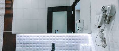 A modern bathroom with a large mirror, a white sink, and a hairdryer on a wall-mounted stand.