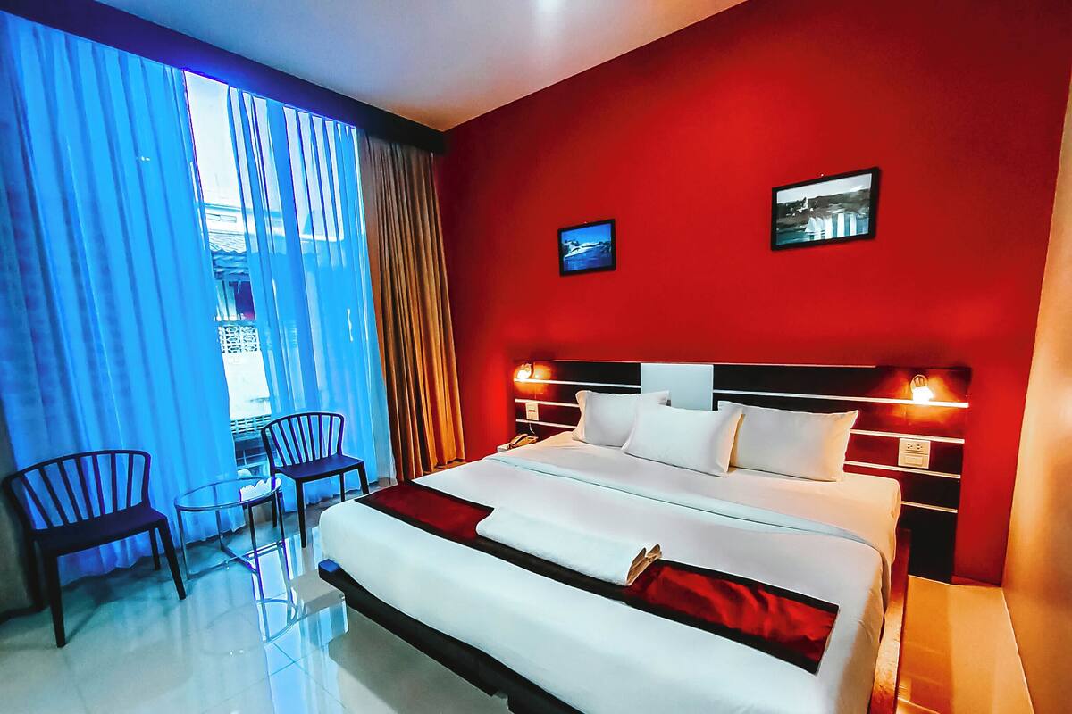 Una habitación de hotel con una cama grande, un escritorio, dos sillas, un televisor y una pared decorada en rojo.